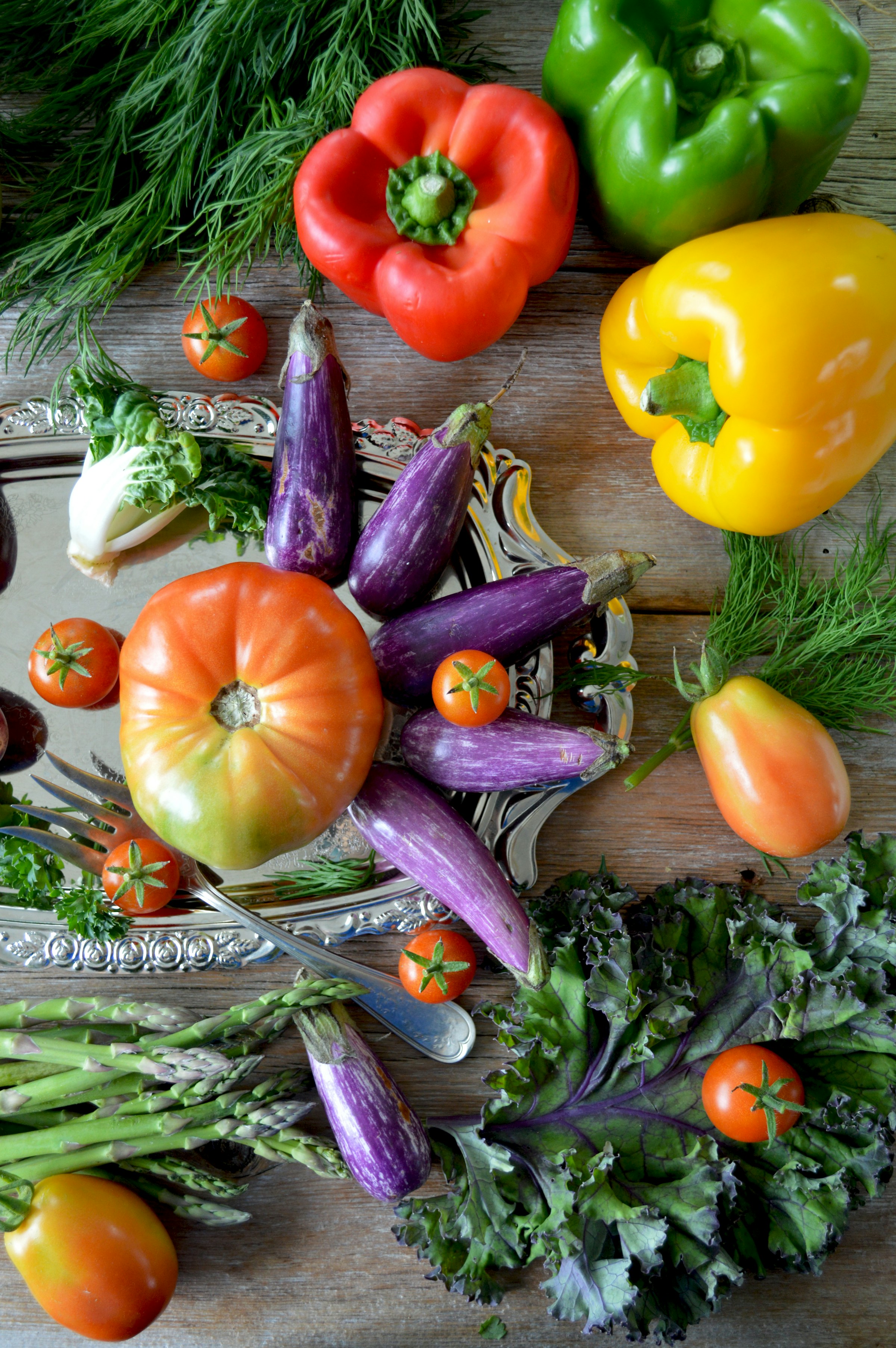 Sesonggrønnsaker arrangert på et rustikt bord med paprika, aubergine, tomater og urter